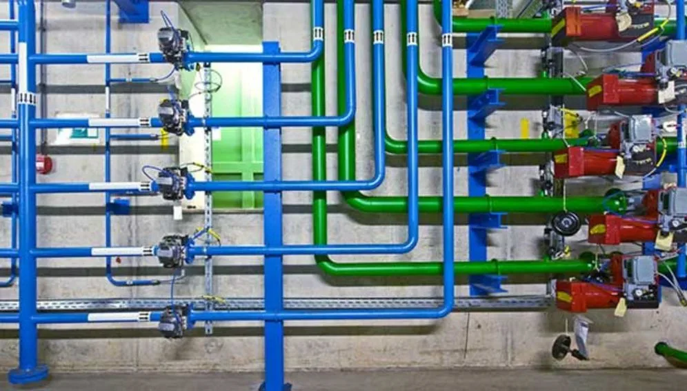 Sistema hidráulico com tubulações industriais azuis e verdes interligadas a bombas vermelhas.